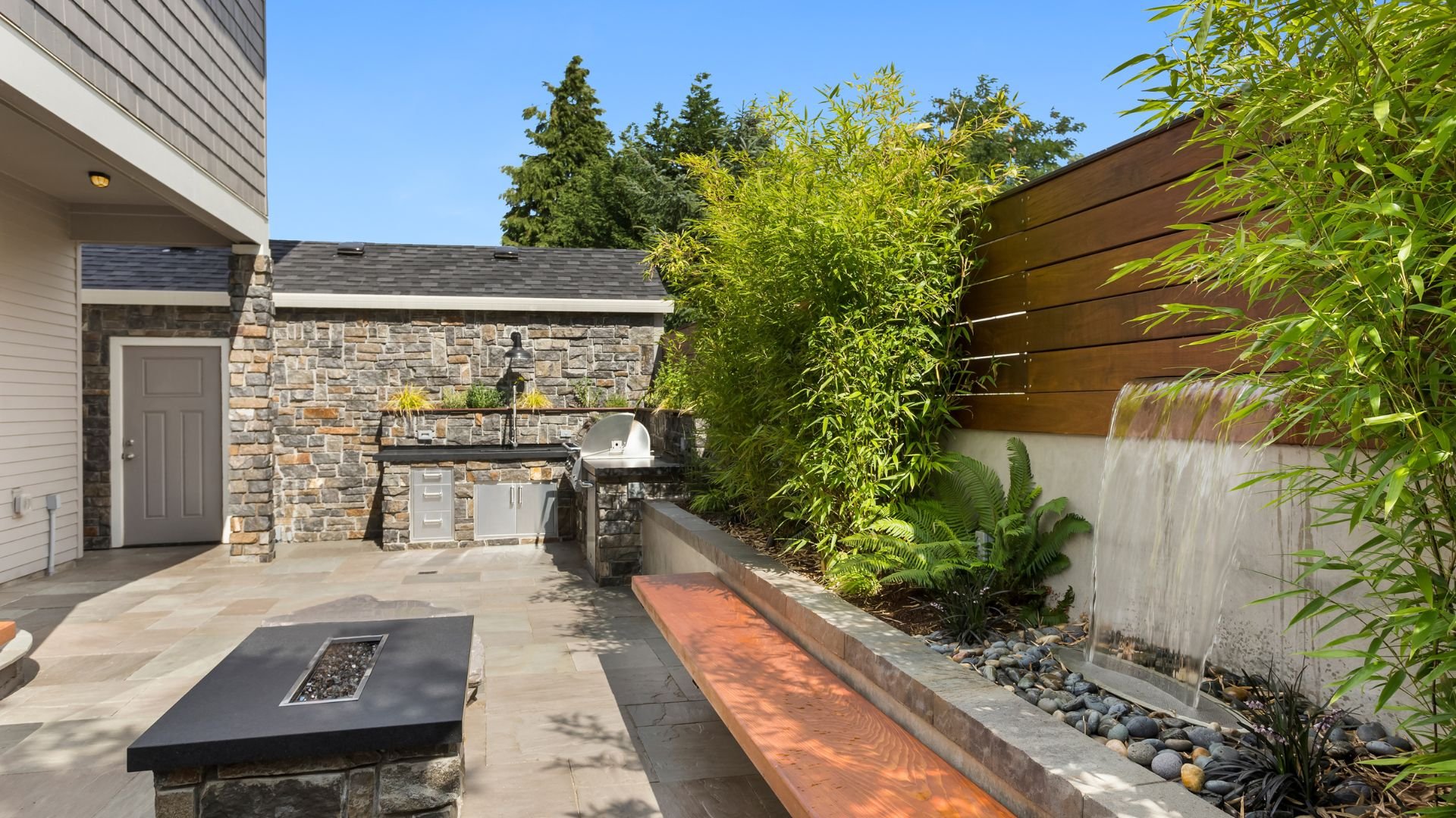 Modern outdoor kitchen with waterfall, grill, and lush green landscaping
