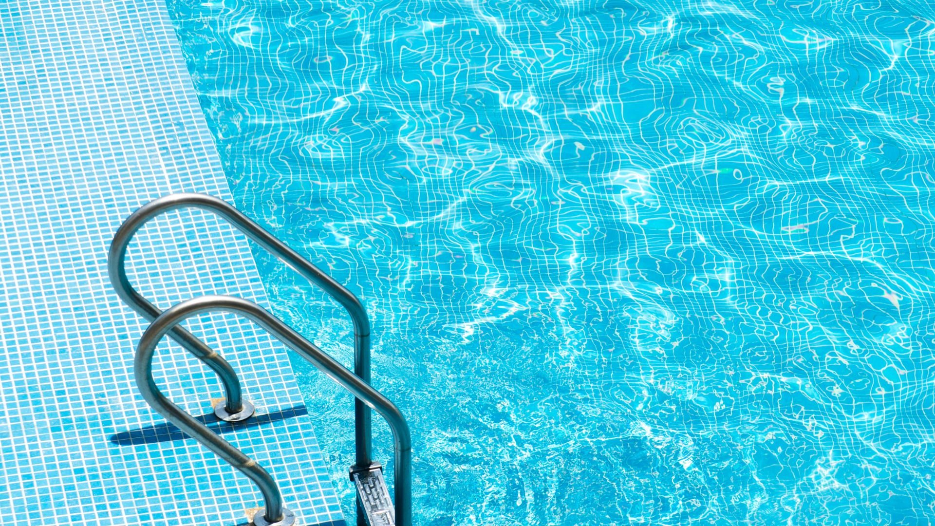 Swimming pool with clear blue water and metal ladder on tiled deck
